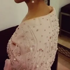 The back and shoulder detail of the pink gown shows how the intricate embroidery continues around the piece. The off-shoulder design is finished with soft bows for a romantic touch.
