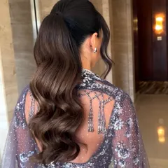 A chic and modern high ponytail with soft, flowing waves. This style is perfect for keeping hair off the face while still showing off its length and volume, making it a great choice for a Sangeet or reception.