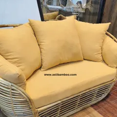 A close-up of our two-seater rattan sofa, complete with plush, mustard-yellow cushions. The curved frame and sturdy weave demonstrate the comfort and durability of our handcrafted furniture, ideal for compact living spaces.
