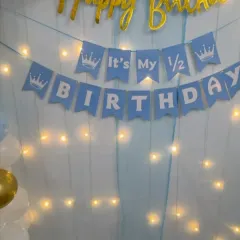 For smaller, more intimate celebrations, I can create a simple yet beautiful backdrop like this one. It features a blue curtain with fairy lights and a "It's My 1/2 Birthday" banner.