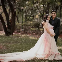 An enchanting portrait of an expecting couple enjoying a quiet moment together outdoors. The long train of the gown spreads out on the grass, adding a touch of romance to the scene.