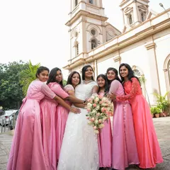 A fun and loving moment between the bride and her bridesmaids, all dressed in matching pink gowns, outside the church.