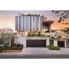The facade of the House Above The Tree captured at sunset, showcasing how the structure interacts with light. We used clean lines, a rooftop garden, and distinctive vertical louvers to create a modern home that is both private and open to its surroundings. This view highlights the home's strong geometric form against the soft evening sky.