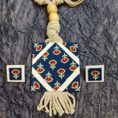 A simple and elegant design featuring blue block-printed fabric with a red floral motif. The square pendant is complemented by a macrame-style cord and tassel, giving it a soft, handcrafted feel. The small matching earrings make it a lovely set for daily wear.