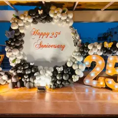 An elegant 25th-anniversary party on a rooftop. This setup features a circular backdrop with custom text, a black and silver balloon garland, and large marquee numbers.