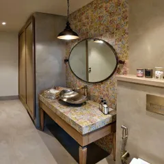This powder room is a delightful mix of patterns and textures. A vibrant floral wallpaper and matching countertop are balanced by the smooth, cool finish of the lime-plastered walls and a simple wooden vanity.