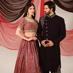 A shot from a professional ethnic wear photoshoot. The model is wearing a deep wine-colored Indo-western sherwani with intricate silver embroidery on the shoulder and cuff.