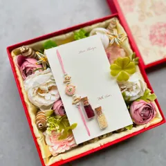 The inside of one of our Rakhi gift boxes, featuring a beautiful Rakhi and Lumba set on a personalized card, surrounded by a bed of artificial flowers and traditional Roli Chawal vials.