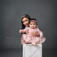 A playful moment between sisters, with the older one giving her baby sister a loving hug.