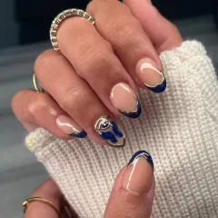 A modern twist on a French manicure, featuring a deep blue tip with a hand-painted gold outline and a 3D abstract blue and gold accent nail.