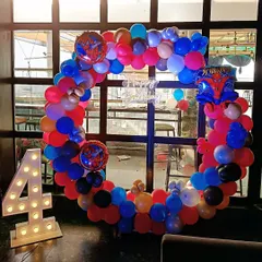 A vibrant Spiderman-themed 4th birthday party. The decoration features a circular balloon arch in classic Spiderman colors and a large light-up number '4'.