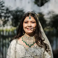 A close-up of pure bridal radiance. The intricate mirror work and gotta pati detailing on this ivory lehenga catch the light beautifully, framing her happy smile.