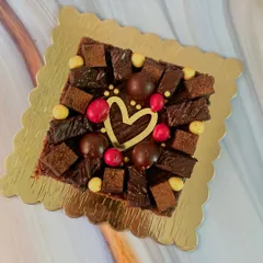 All your cravings in one bite. This brownie cake is lavishly decorated with brownie pieces, chocolate balls, and colorful candies, with a golden heart at the center.