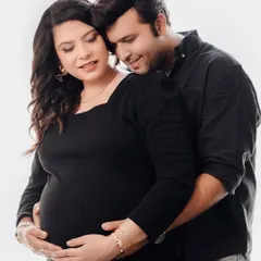 A warm and affectionate studio portrait of an expecting couple. The partner embraces the mom-to-be from behind, both sharing a gentle smile, creating a feeling of comfort and love.