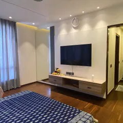 This master bedroom in Noida features a floating TV unit and warm wooden flooring. The design is clean and minimalist, creating a spacious and relaxing atmosphere.
