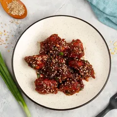 Our saucy Sesame Chicken, seen from a top-down angle. Bite-sized chicken pieces are coated in a thick, dark, and savoury sauce and generously sprinkled with sesame seeds.
