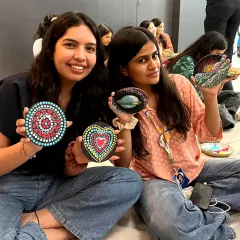 Two colleagues display the beautiful mandala dot art they created on stones during a team-building session. It's a relaxing and mindful activity perfect for de-stressing.