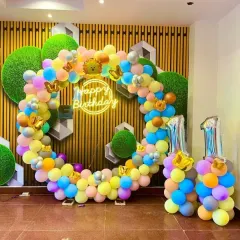 We create modern and vibrant first birthday decorations like this one. The setup features a colorful, asymmetrical balloon hoop, a custom 'Happy Birthday' neon sign for a trendy touch, and large '1' foil balloons to mark the special milestone. This style is perfect for a lively and stylish party.