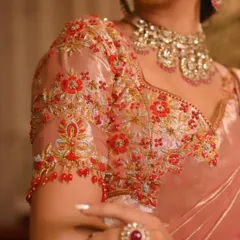A detailed shot of a hand-embroidered blouse sleeve in a beautiful peach-pink tissue silk, adorned with red and gold threadwork.