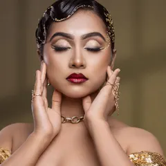 This close-up showcases the intricate eye makeup and the flawless, glowing skin. The gold leaf detail in the hair adds an extra touch of editorial flair.