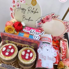 A beautiful Rakhi hamper designed to make your sibling feel blessed. This tray includes decorated jars, snacks, a drink, and a custom "Happy Raksha Bandhan" sign, all arranged with floral accents.