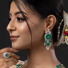 A close-up profile shot focusing on the intricate details of the emerald earrings and maang tikka from the bridal set.