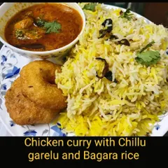 A traditional Hyderabadi combination of Bagara rice served with chicken curry and crispy chillu garelu (vada with a hole).