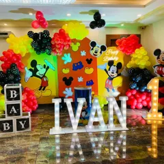 A classic Mickey Mouse themed first birthday for baby Ivan. The setup includes large marquee letters, character backdrops, and balloon arrangements in Mickey's signature red, yellow, and black colors.