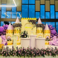 This Rapunzel-themed castle setup for a first birthday features her signature purple and gold colors, complete with a tower, floral decorations, and a matching carriage prop.