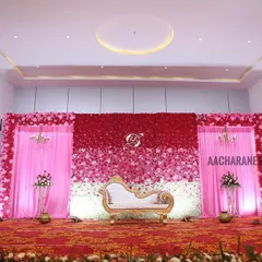 This reception stage features a beautiful ombre flower wall, transitioning from deep red to pink and finally to white. The design is framed by elegant pink drapes and chandeliers, creating a romantic and colorful setting for the couple.