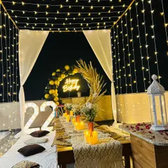 This angle showcases the ceiling of fairy lights that creates a starry night effect for this terrace cabana setup. The arrangement includes large '22' marquee numbers and a white lantern for added ambiance.