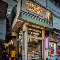 The exterior of Shiv Mishthan Bhandar at dusk. The material palette, including red stone and lakhori bricks, was inspired by the architecture of Chandni Chowk's havelis to ground the modern storefront in its context.