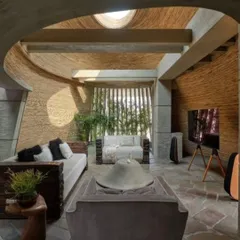 This living space features walls with a textured, brick-like finish and a ceiling of exposed bamboo. A circular skylight brings in natural light, highlighting the honest materials and creating a warm, earthy atmosphere.