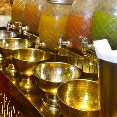 A close-up of our exclusive chaat catering setup. Gleaming brass bowls are lined up next to glass dispensers filled with tangy and spicy waters, ready for creating delicious pani puri.