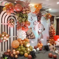 A sweet Teddy Bear theme for a 5th birthday party. The decor uses a warm, earthy color palette of olive green, brown, and orange balloons, with a backdrop featuring adorable bear illustrations.