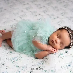 This little one is dreaming sweet dreams in a lovely mint-colored dress. The gentle smile on a sleeping newborn's face is one of the most precious things to capture.