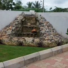 A custom-built rock waterfall feature against a boundary wall. This type of water feature can mask unwanted noise and create a soothing ambiance in any garden.
