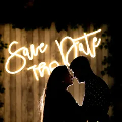 A classic "Save the Date" silhouette. The couple is framed against a neon sign, creating a modern, stylish, and intimate announcement photo.