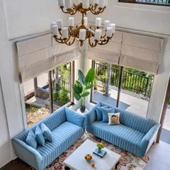 An aerial view of the double-height living room, highlighting the grand chandelier, plush blue sofas, and large windows that flood the space with natural light.