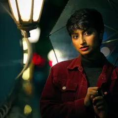 A moody, cinematic portrait of a woman with short hair holding an umbrella under a glowing streetlamp at night. The rich colors and soft focus on the background city lights create a story-driven atmosphere.