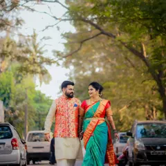 A full-length shot of a couple in vibrant Maharashtrian traditional attire, walking down a tree-lined street. This blends tradition with a modern, urban setting.