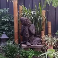 This Zen garden corner features a resting Buddha statue set against a backdrop of natural bamboo poles. The mix of grasses and ferns adds to the serene, contemplative feel.