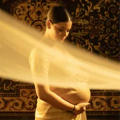 A moment of deep connection. The mother-to-be, draped in a beautiful saree, cradles her belly. The sheer fabric and warm lighting create a soft, ethereal glow, highlighting the sacred bond between mother and child.