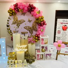 I love creating magical first birthday setups like this butterfly theme. It features a large circular backdrop with golden butterflies, a pink and gold balloon garland, a light-up marquee '1', illuminated name and 'BABY' blocks, and a personalized milestone board detailing the baby's first year.