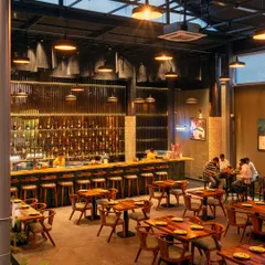 The main dining area looking towards the bar. The dark steel grid ceiling conceals services while providing a structure for the industrial pendant lights. The combination of custom wooden chairs and tables adds a rustic touch that balances the industrial design.