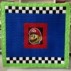 It's-a-me, Mario! This Super Mario themed quilt is perfect for any young gamer, featuring a large appliqué of Mario's face, a checkerboard border, and wavy quilting to mimic movement.