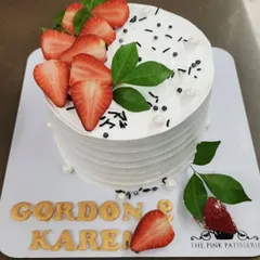 A simple and elegant white cake with a textured finish. It's beautifully topped with freshly sliced strawberries and green leaves for a clean and fresh look.