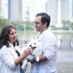 A serene family portrait in Singapore, with the city skyline in the background, capturing a quiet moment of connection between a couple and their white Japanese Spitz.