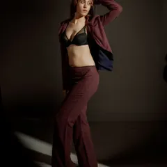 A full-length studio shot demonstrating how lighting can define a space. The sliver of light on the floor grounds the model, drawing attention to her confident stance and the flow of the wide-leg trousers.