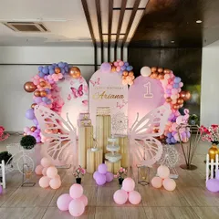 An enchanting butterfly garden for Ariana's first birthday. This large-scale indoor setup features multiple backdrops, large wing props, and balloon garlands in shades of pink, purple, and rose gold.
